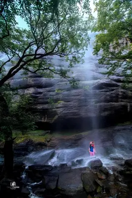 a woman is standing in front of a waterfall at Honeyrock Farm Resort by Skybz in Kanthalloor