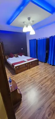 a bedroom with two beds and a table and blue curtains at Romanzia Village Homestay in Mānantoddy