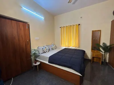 a bedroom with a bed with a blue comforter and a window at Hamsa Farmstay Mysore, Campfire, Bbq, Cricket in Mysore
