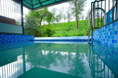 a swimming pool with blue tiles and a view of a hill at Private Pool Villa by Green View in Vythiri