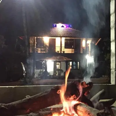 a group of people around a fire in front of a building at Kund estate stay in Madikeri