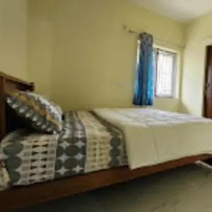 a bedroom with a bed and a window with blue curtains at Sai Home Stay in Marudhamalai