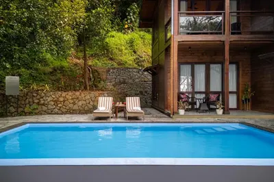 a pool with two chairs and a table and a house at amã Stays & Trails - Iris Villa, Kozhikode in Puthuppādi