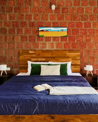 a bedroom with a blue bed with a brick wall at Nila by Raho - Secluded Villa with Estate View in Siddapur