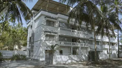 a white building with palm trees in front of it at Hotel Spacio in Kozhikode