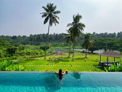 a woman in a swimming pool with a view of a resort at Pollachi Riverhouse, A CGH Earth Saha experience in Pollāchi