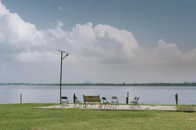 a group of chairs and a bench by the water at Discovery Village Kabini in Antarasante