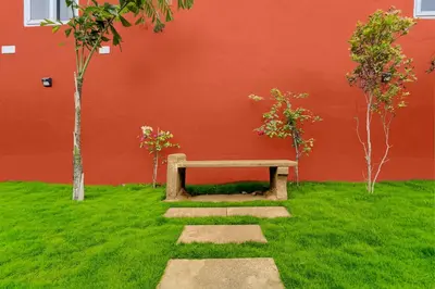 a bench sitting in the grass next to a red wall at Palette Mithalai Farm by CheckIn | Garden | Pvt Pool | Coimbatore in Coimbatore