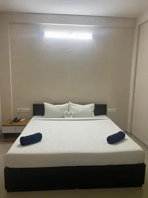 a large white bed with two blue pillows on it at Neurogreen Apartments in Kottakkal