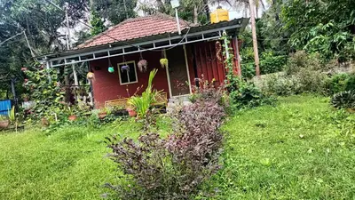 a small red house in a field of grass at Manna Homestay coorg in Kushālnagar