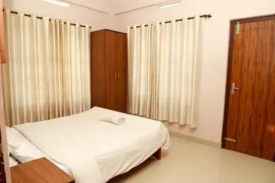a bedroom with a bed with white sheets and wooden cabinets at Fine Homes in Kalpetta