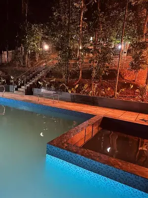 a swimming pool at night with benches in the water at SURAAS Homestay Vythiri in Vythiri