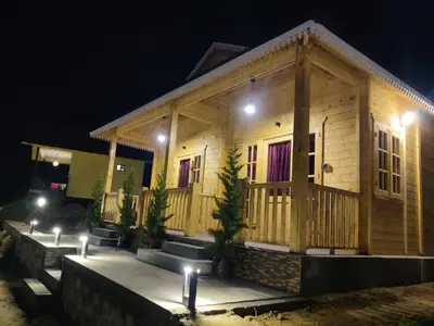 a wooden house with lights in front of it at night at Cloudy Nandy Hills Poombarai in Kūkkāl