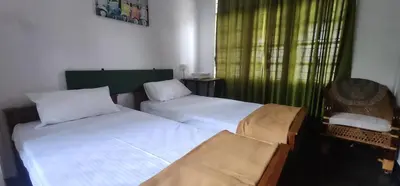a bedroom with two beds and a window with green curtains at Kodamukku cottage in Trichūr