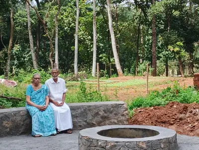 a man and woman sitting next to a stone fountain at The Cool Cottage at gaya3farms in Palakkad
