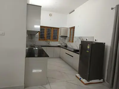 a white kitchen with a black refrigerator in it at Aathira Agri Homes in Trichūr