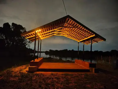 a wooden pavilion with lights on top of a body of water at Anava Farms in Shrīrangapattana