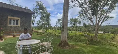 a man standing next to a table in a yard at Nadhi Teera Riverside Stay in Kushālnagar