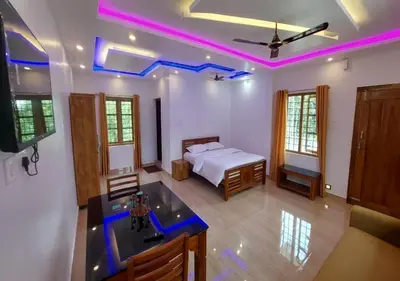 a bedroom with a bed and a kitchen with purple lights at Carmel Cottage in Marayoor
