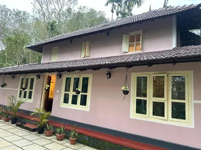 a pink house with white windows and plants at Bucolic Resort in Panamaram