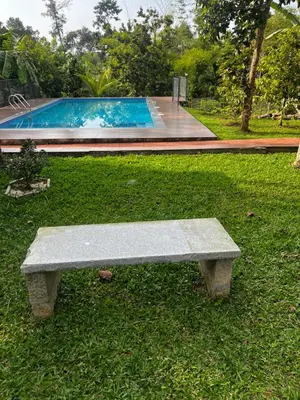 a stone bench sitting in the grass near a swimming pool at Avocado Orchards - Villa in Kenichira