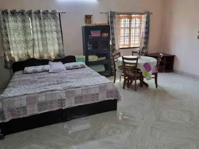 a bedroom with a bed and a table and a chair at Brindavanam HomeStay Salem in Salem