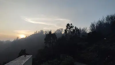 a view of the sun rising over a mountain with trees at The Dew Nest in Ooty