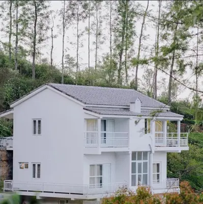 a white house with a balcony and trees at Prithivee Homestay in Kotagiri