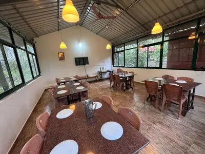 a dining room with tables and chairs and windows at Manuvan Estate Stay in Kushālnagar