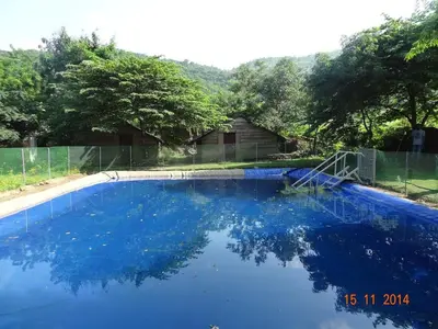 a blue swimming pool with a fence and trees at Tranquilandia in Varagampadi