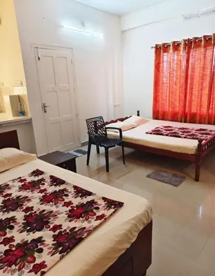 a room with two beds and a chair in it at Darshanam Inn in Guruvāyūr