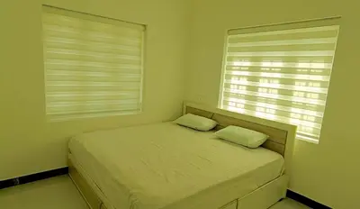 a bedroom with a bed with two pillows and two windows at White Cloud Stay Attappadi in Agali