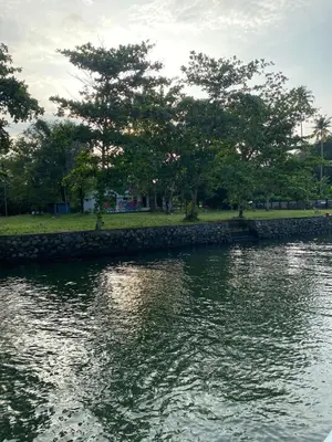 a river with a stone wall and trees in a park at Some where Else Musiris Heritage in Parūr