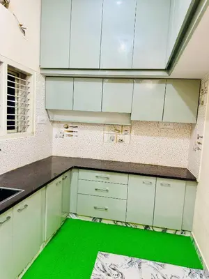 a kitchen with white cabinets and a green floor at Flats in CITY Centre Next to Nexus Mall, 1km from bus stand in Mysore
