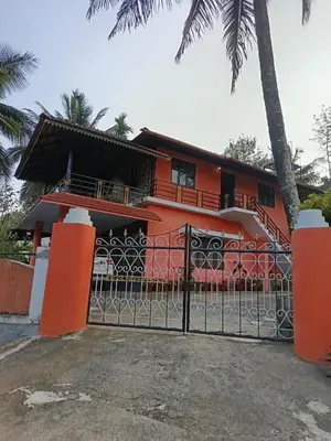a orange house with a gate and palm trees at Ananya Homestay in Napoklu