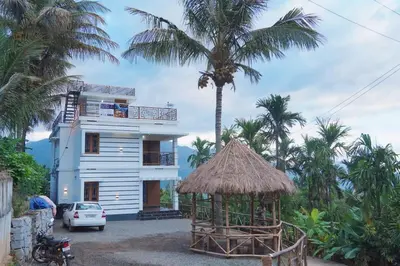 a white house with a palm tree and a building at Paalm view premium resort in Kanthalloor