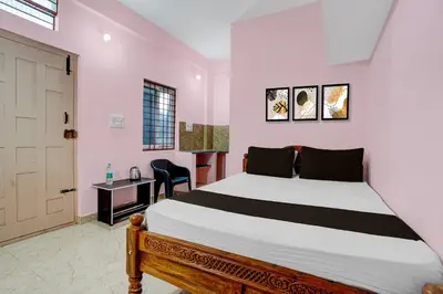 a bedroom with a bed and a desk and a door at Hotel O Nimishamba Residency in Mysore