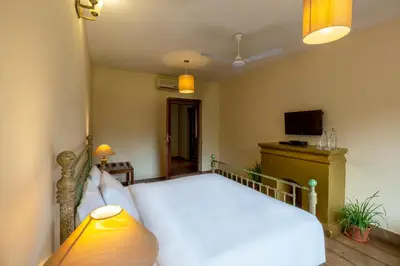 a bedroom with a white bed and a television at amã Stays & Trails - Taneerhulla Bungalow, Coorg in Titimati