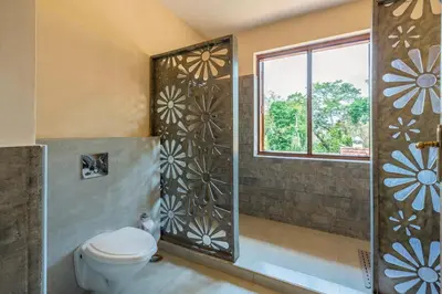a bathroom with a shower with a toilet and a window at amã Stays & Trails - Taneerhulla Bungalow, Coorg in Titimati