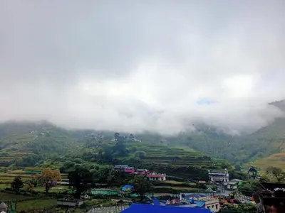 a town on a hill with clouds in the mountains at Vattavada Homestay in Vattavada