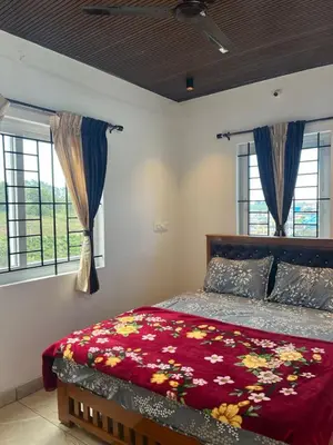 a bedroom with a bed with a red comforter and windows at Village Villa in Vālpārai