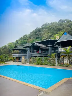 a resort with a blue swimming pool in front of houses at oakden lakkidi villa vythiri villa wayanad in Vythiri