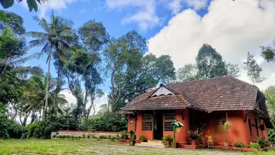a small red house with palm trees in the background at Heritage Mudhouse Homestay in Virajpet