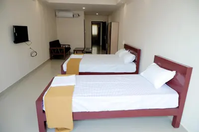 two beds in a small room with a tv at Amritha Lodge in Kollengode