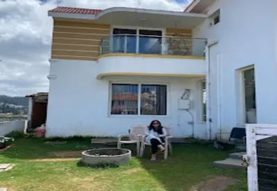 a woman sitting in a chair in front of a house at Palazzo Villa in Ooty
