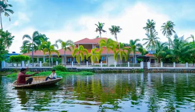 two people in a boat on the water in front of a house at River Whisper Homestay in Cochin