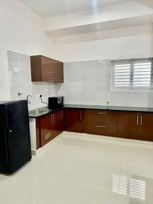 a kitchen with brown cabinets and a black refrigerator at Dakshima Residency in Mysore
