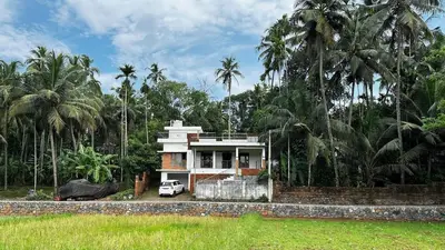 a house in the middle of a field with palm trees at Izzath Villa in Kottakkal