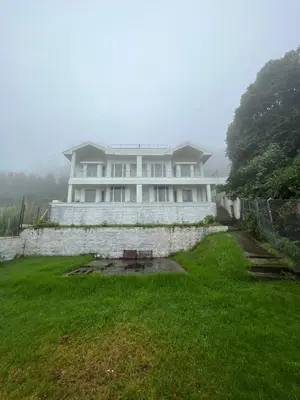 a large white house with a grassy yard in front of it at Hill Side Cottage in Ooty