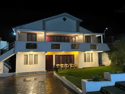 a white house with chairs in the yard at night at Hill Side Cottage in Ooty